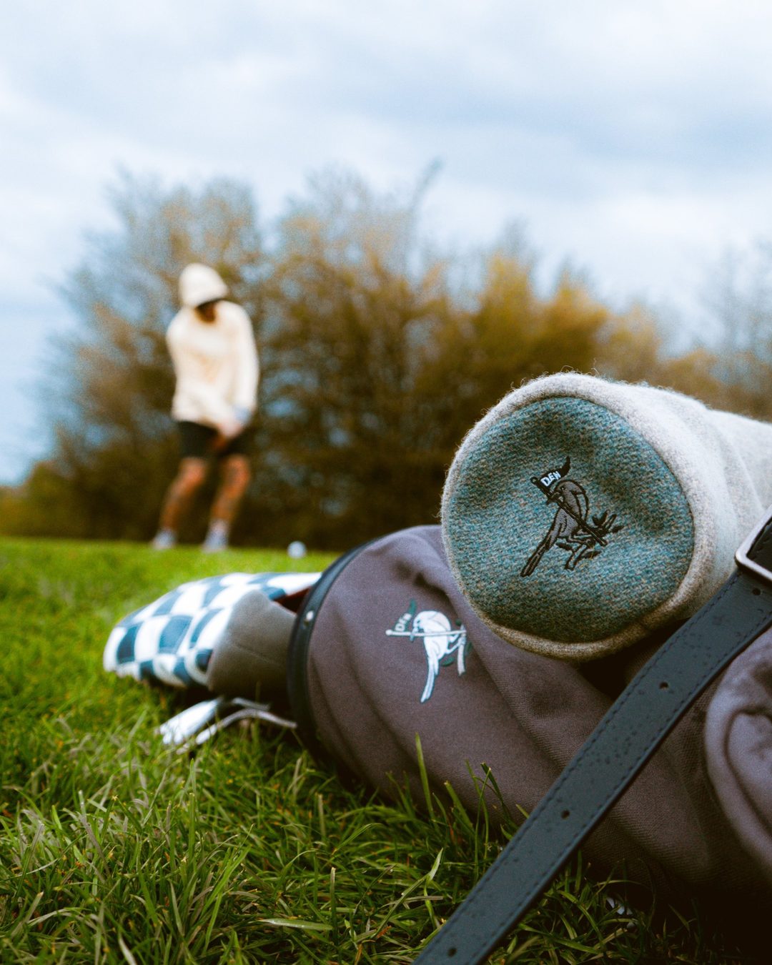 The Magpie x RossCo headcover on a golf bag, a golfer on the tee behind