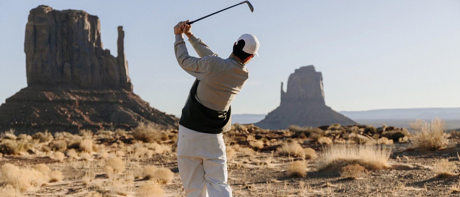 A golfer in a Manors quarter-zip at the finish of a swing in Monument Valley, the Mitten buttes behind him