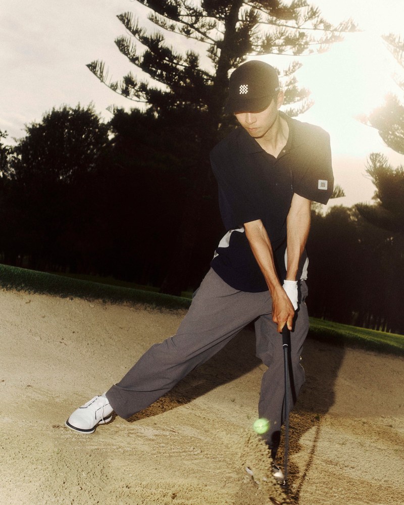A golfer in Manors playing out of a greenside bunker into low evening sun at TPC Sawgrass