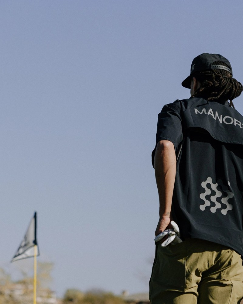 A man in a black Manors caddie bib walking away across a desert course in Arizona