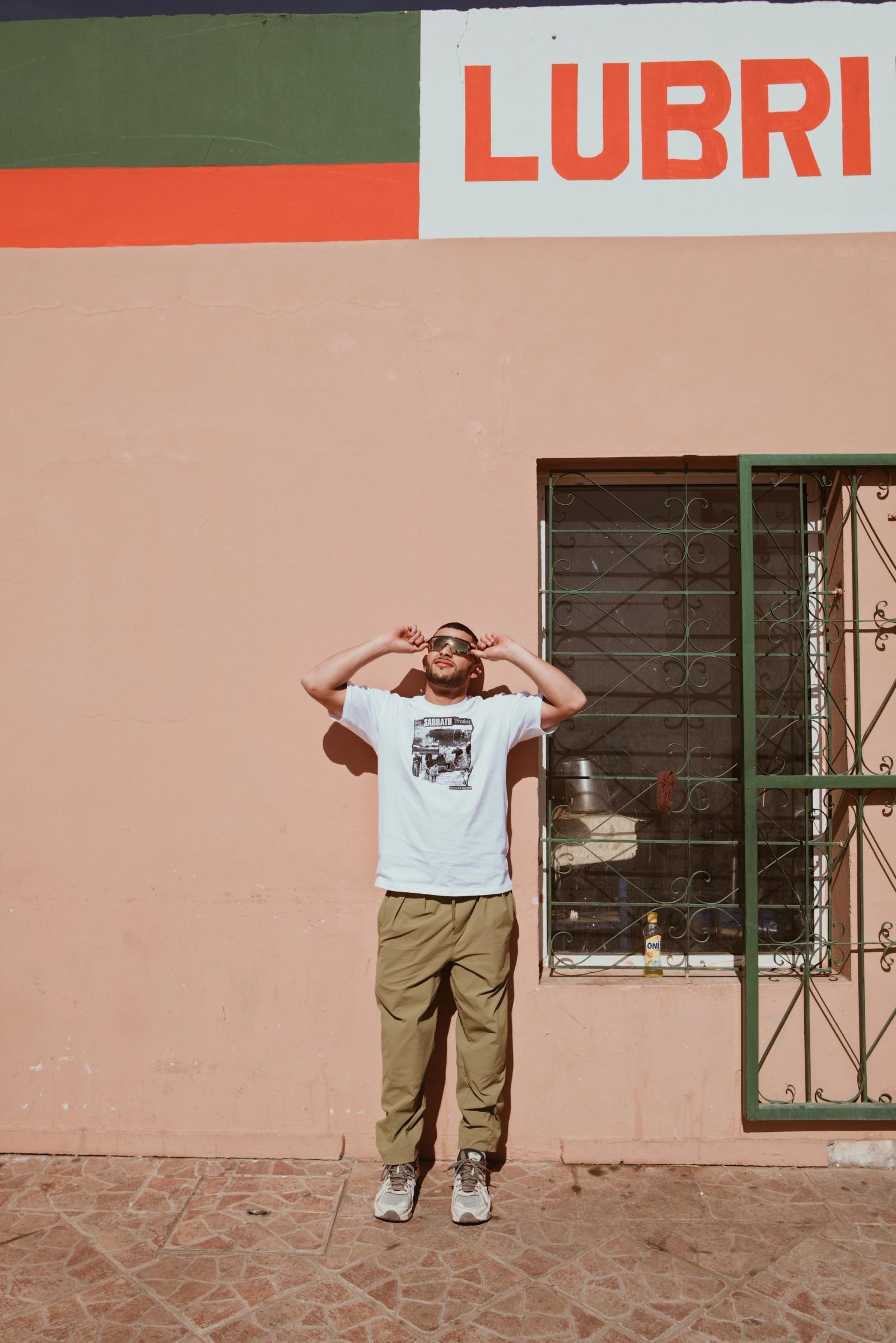 A golfer in a Manors graphic t-shirt standing against a pink painted wall under a LUBRI sign