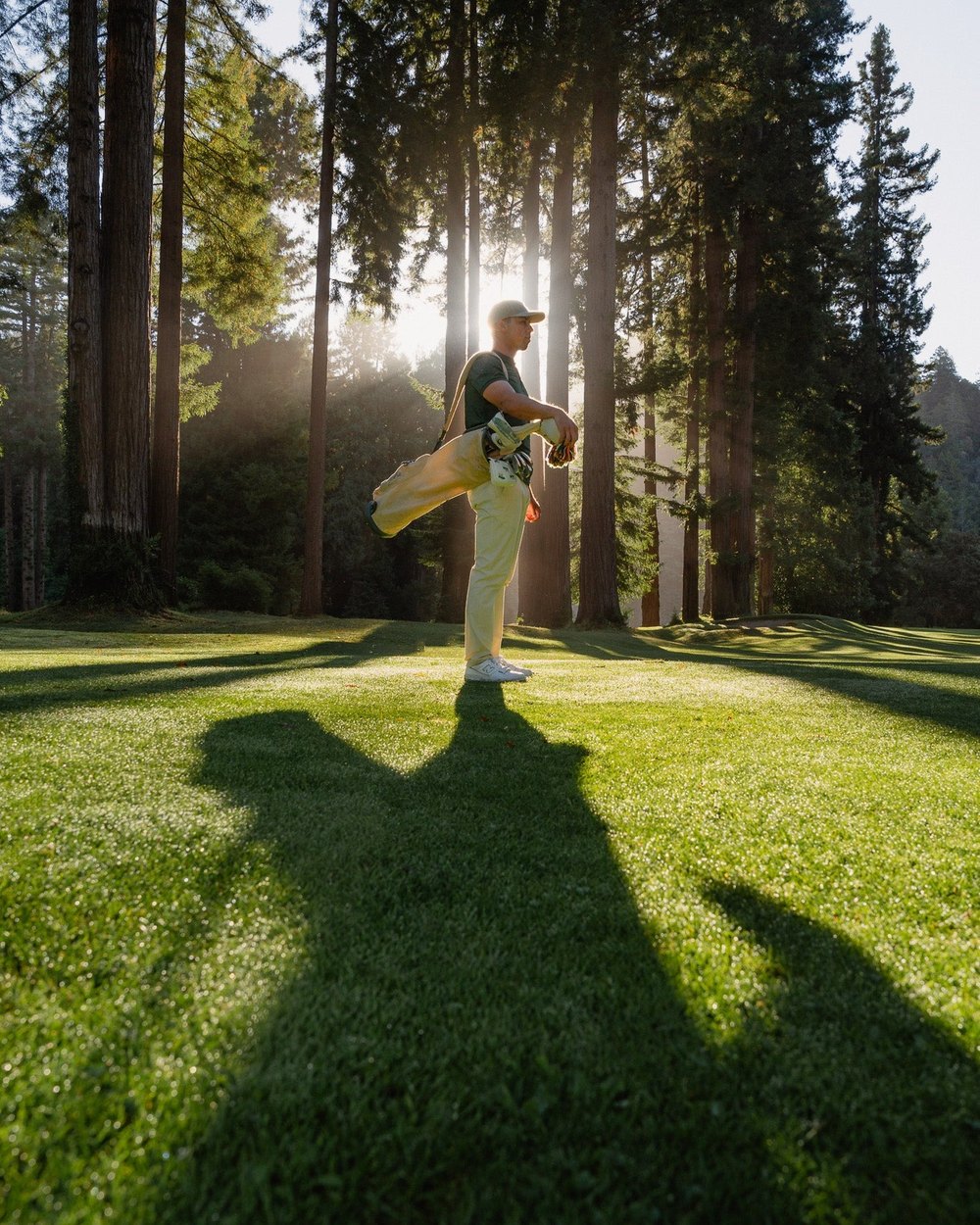 A golfer on a sunlit fairway among redwoods