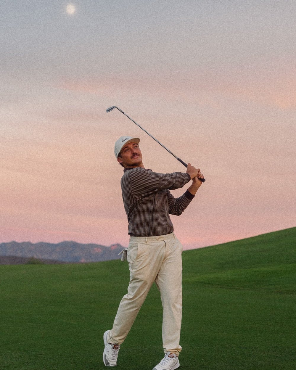 A golfer finishing his swing under a pink dusk sky