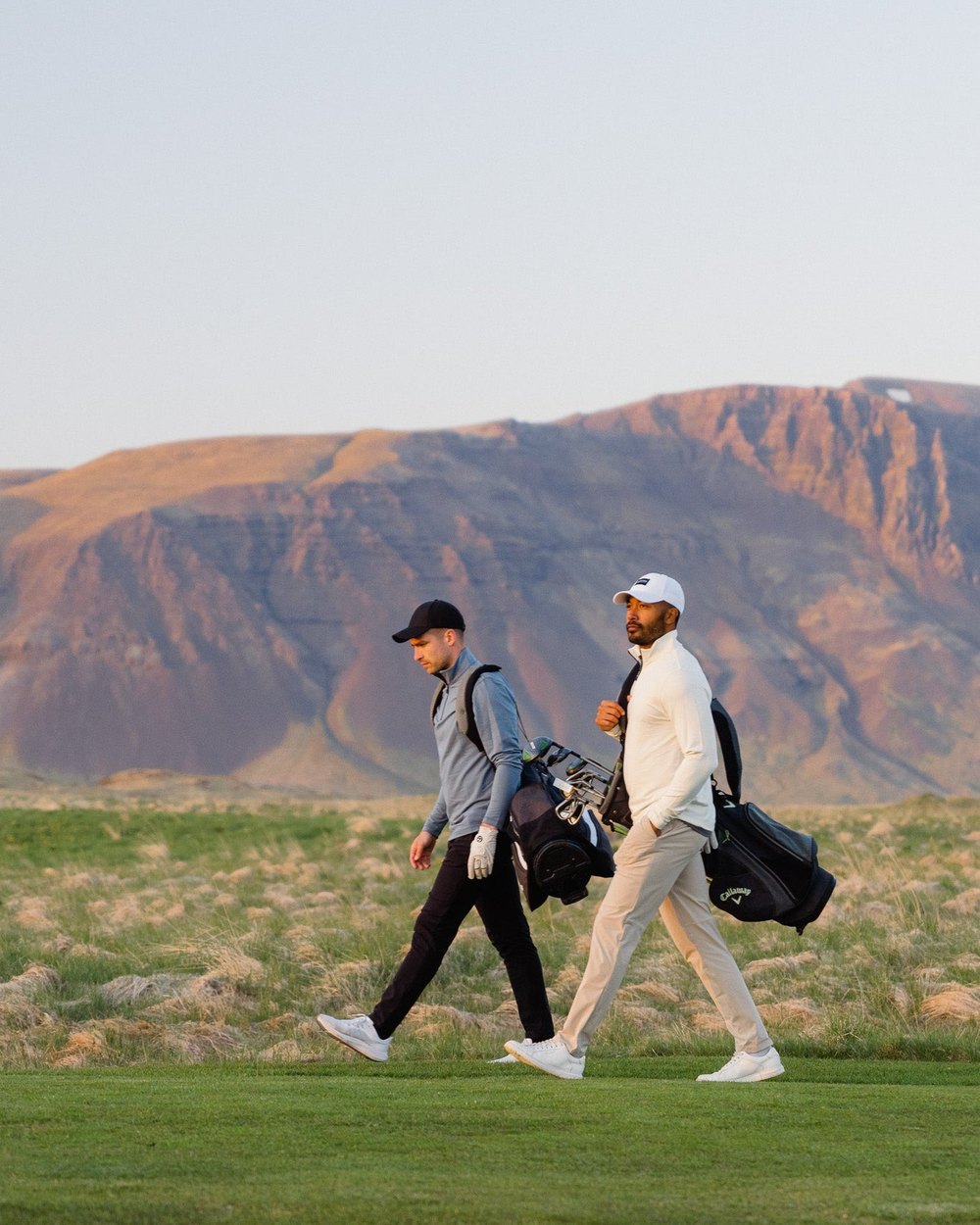 Two golfers walking with carry bags below a red mesa