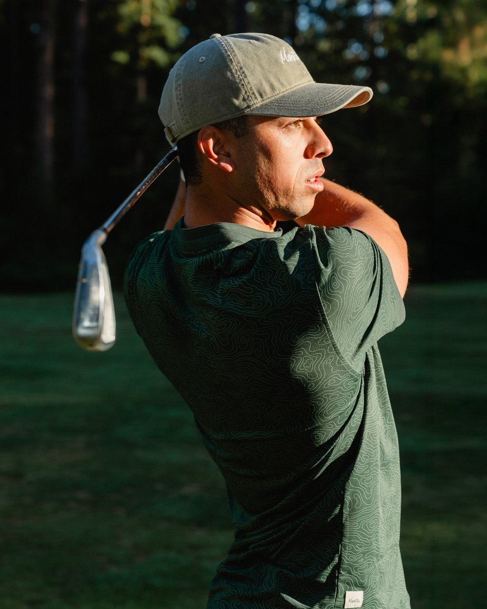 A golfer in a green Catalyst polo finishing his swing