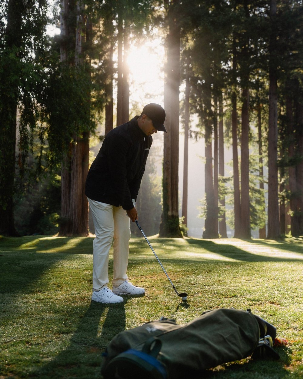 A golfer with a carry bag in a redwood forest clearing