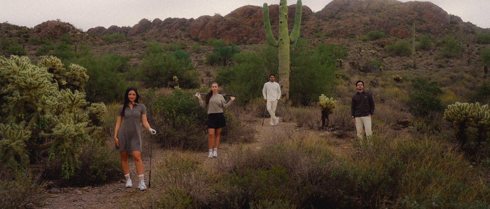 Mantra golfers walking through Sonoran Desert scrub below a saguaro and a rocky ridge