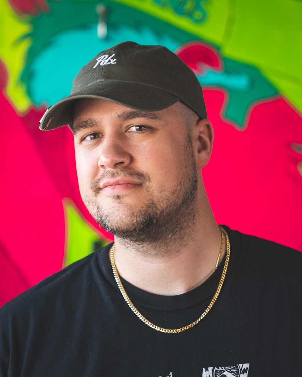 Dane Delgado, founder of Matchstick Golf, in a black cap and gold chain in front of a bright mural