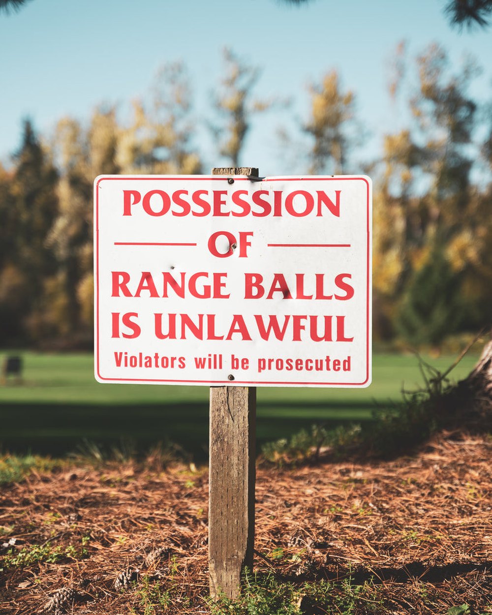 A sign in the trees reading Possession of Range Balls Is Unlawful
