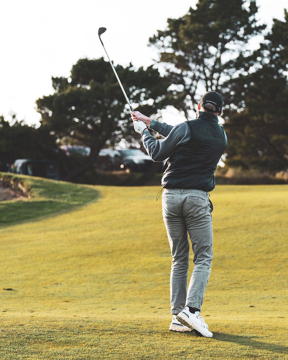 A golfer finishing a swing on a links course at dusk