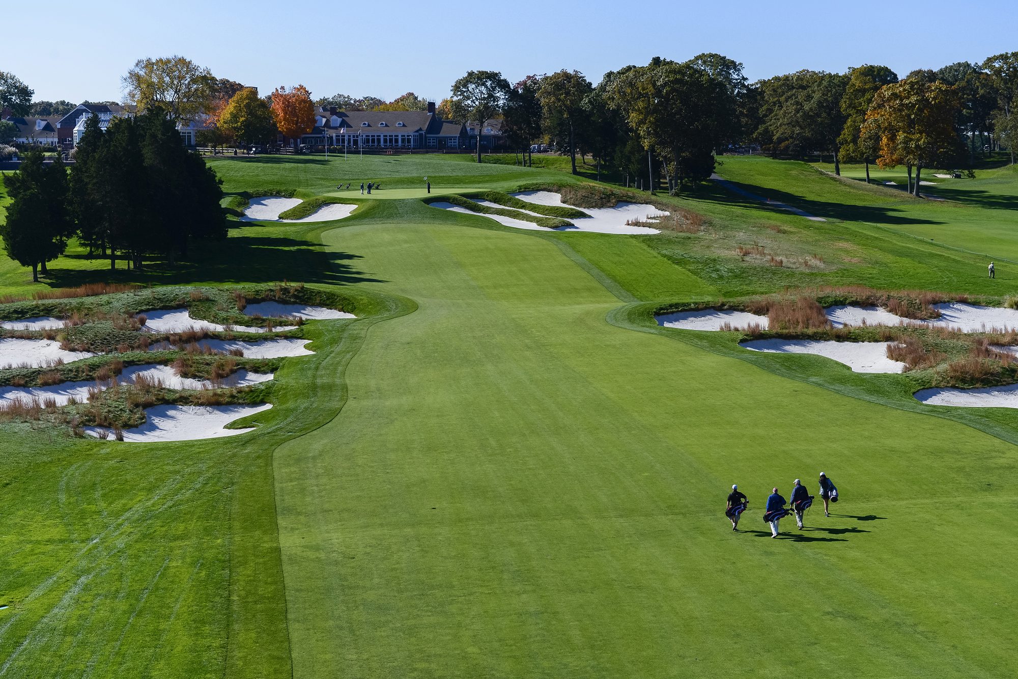 A foursome walking up a broad Bethpage fairway lined with ragged bunkers toward the clubhouse