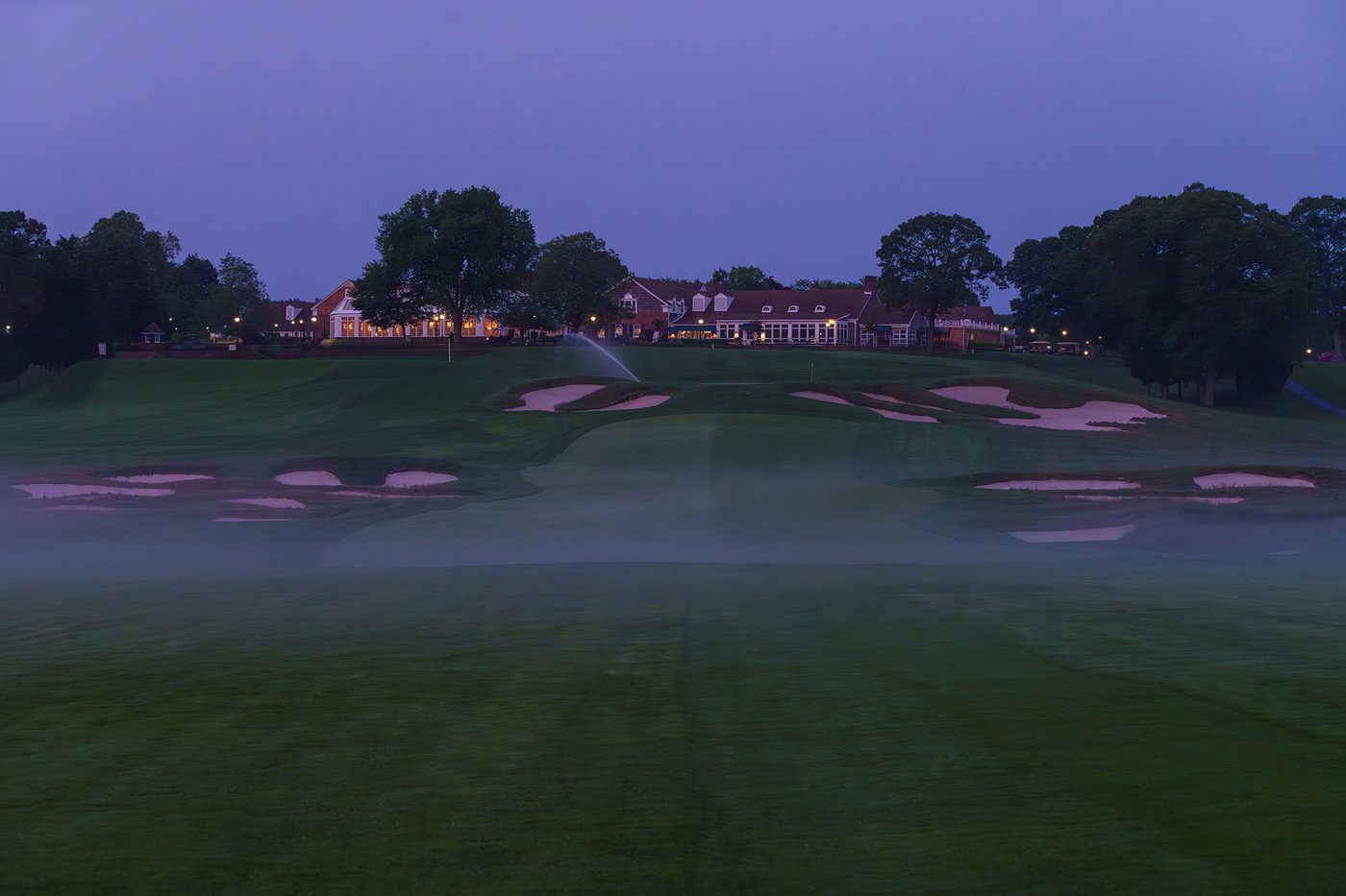 Fog over a bunkered Bethpage fairway at blue hour with the clubhouse lit on the ridge