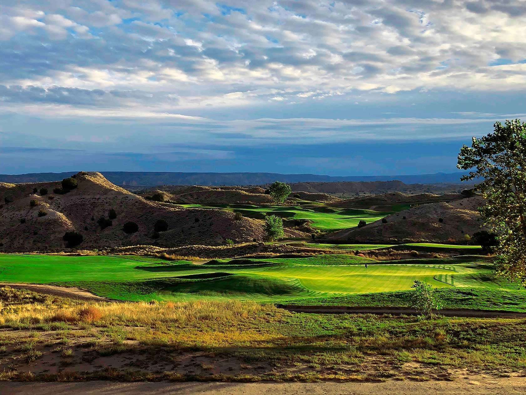 Low golden light across a Black Mesa fairway with eroded badland ridges and a long mesa