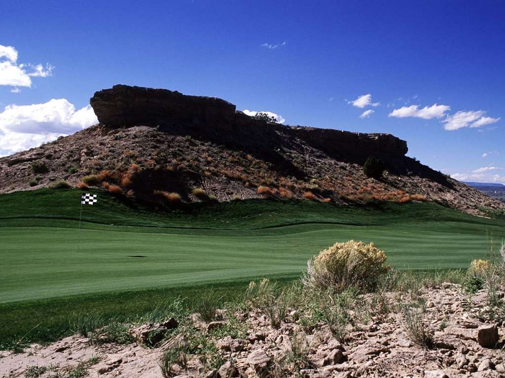 A dark basalt-capped mesa rising over a Black Mesa fairway