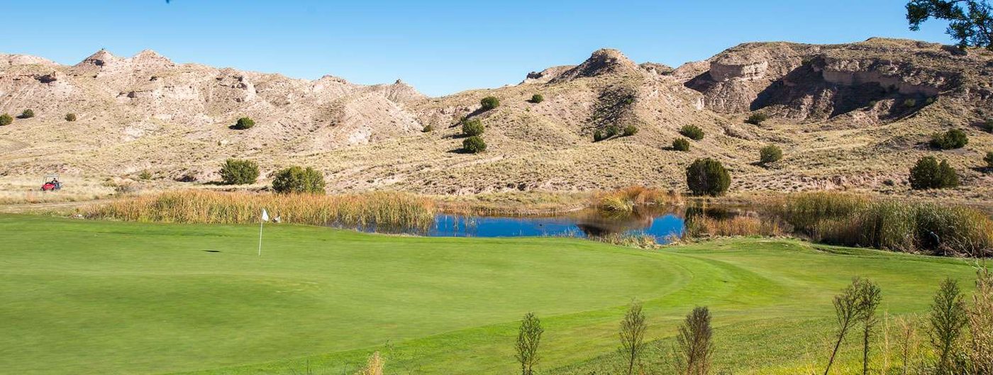 Panorama of a green beside a reed-fringed pond below pale eroded cliffs