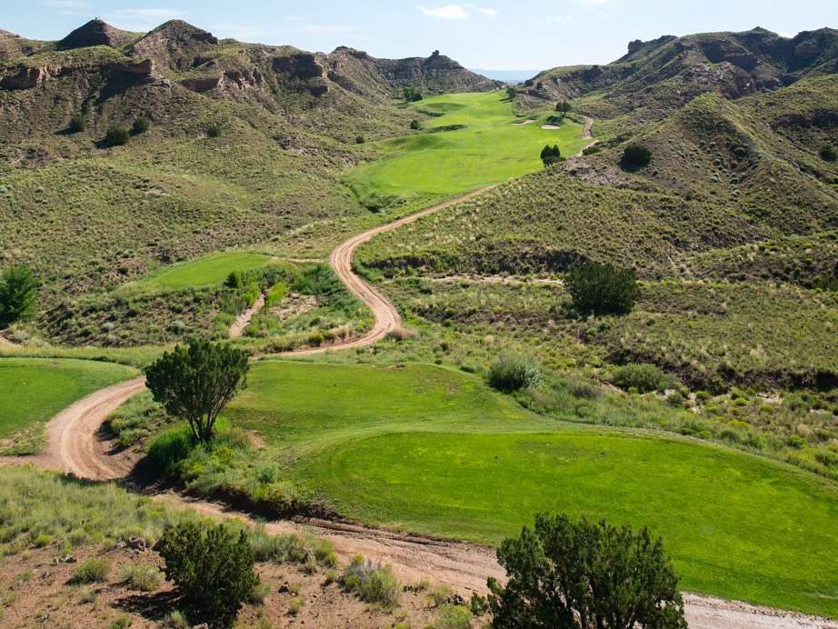 A dirt cart path curling through a green valley between sage-covered hills