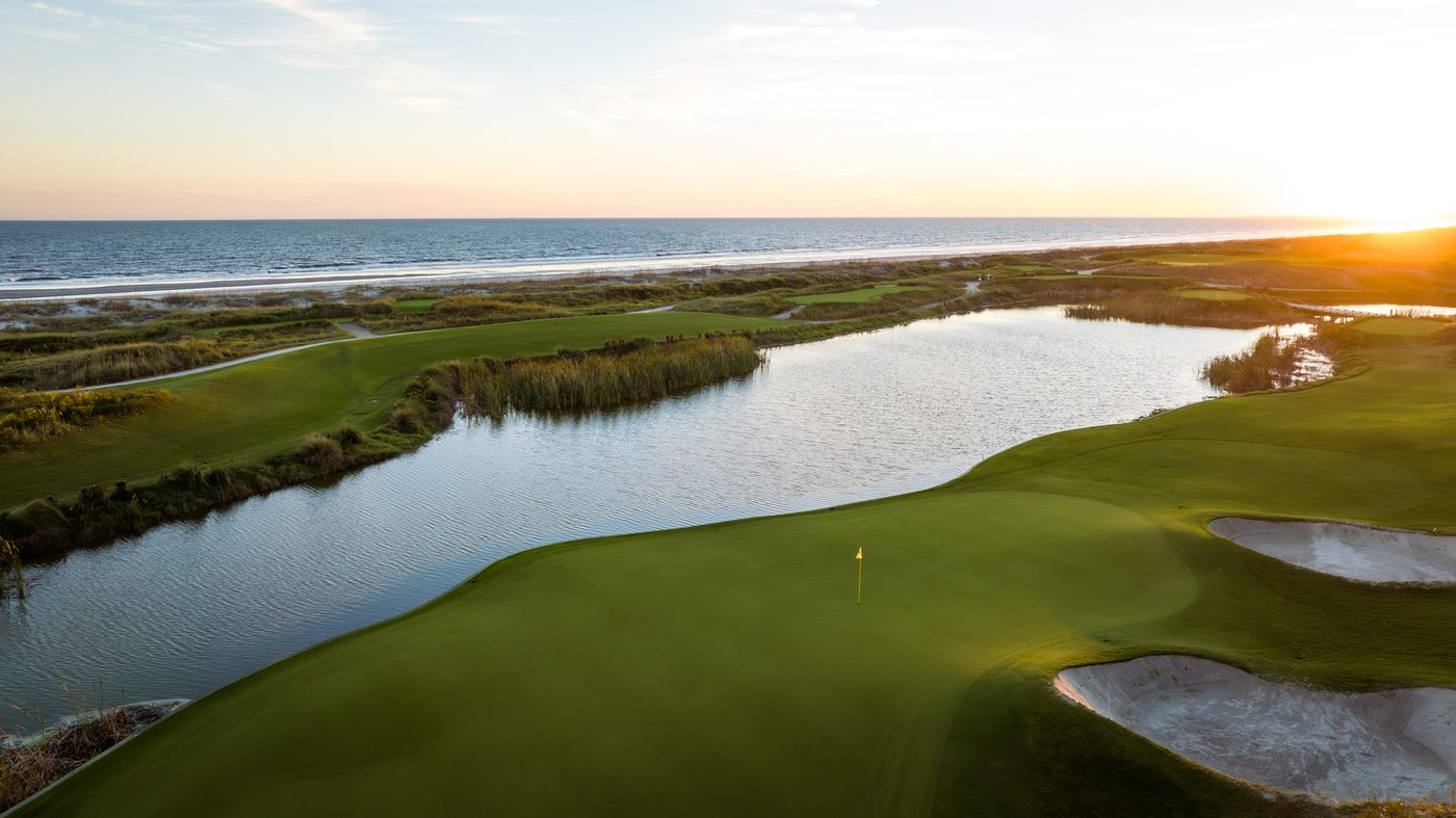 Low sun over the ocean behind a lagoon wrapping a green at Kiawah