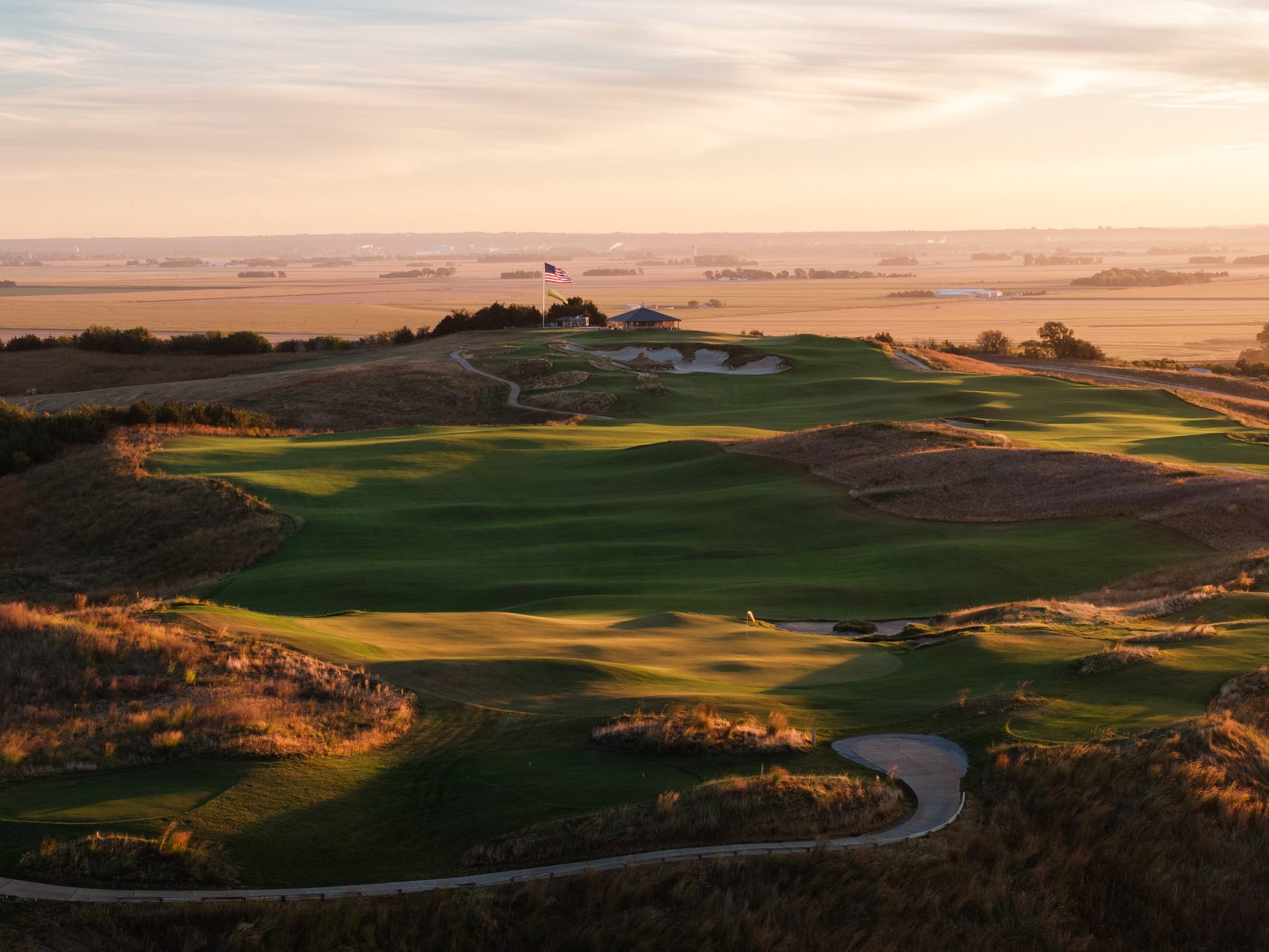 Golden-hour drone view over Landmand's rumpled fairways to the clubhouse on the ridge