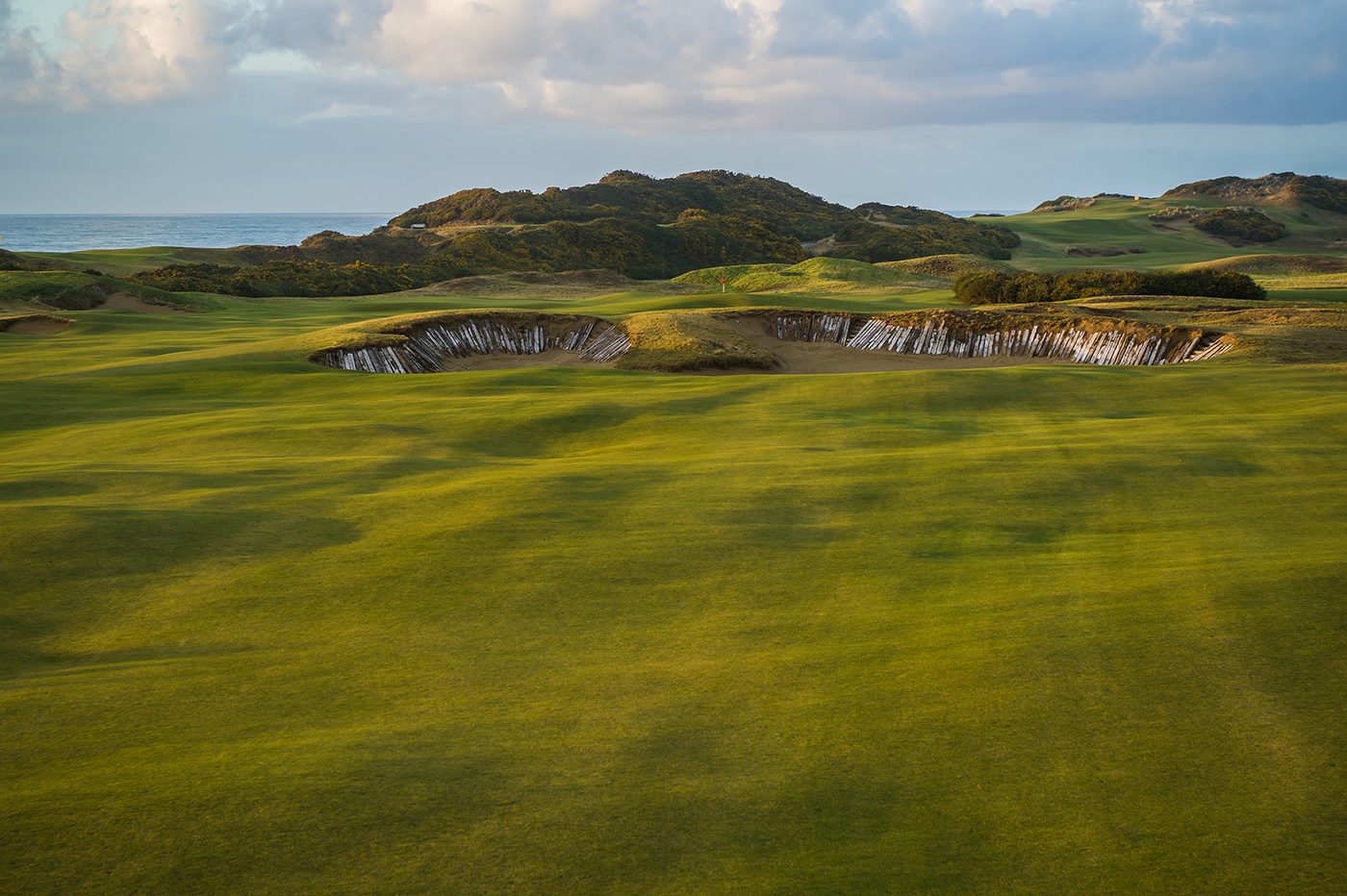 A huge sleeper-faced cross bunker across a wide rolling fairway with the Pacific beyond