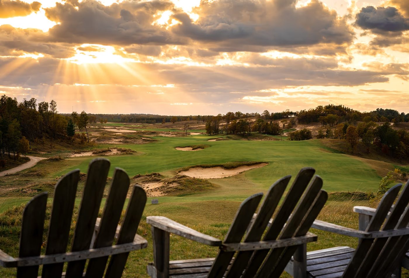 Wooden Adirondack chairs looking over the course as sun rays break through cloud