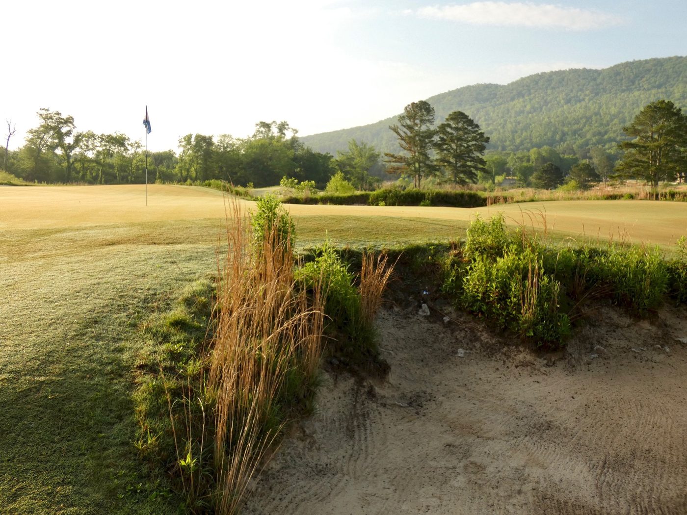 A shaggy-lipped bunker with a flag and green mountain ridges behind at Sweetens Cove