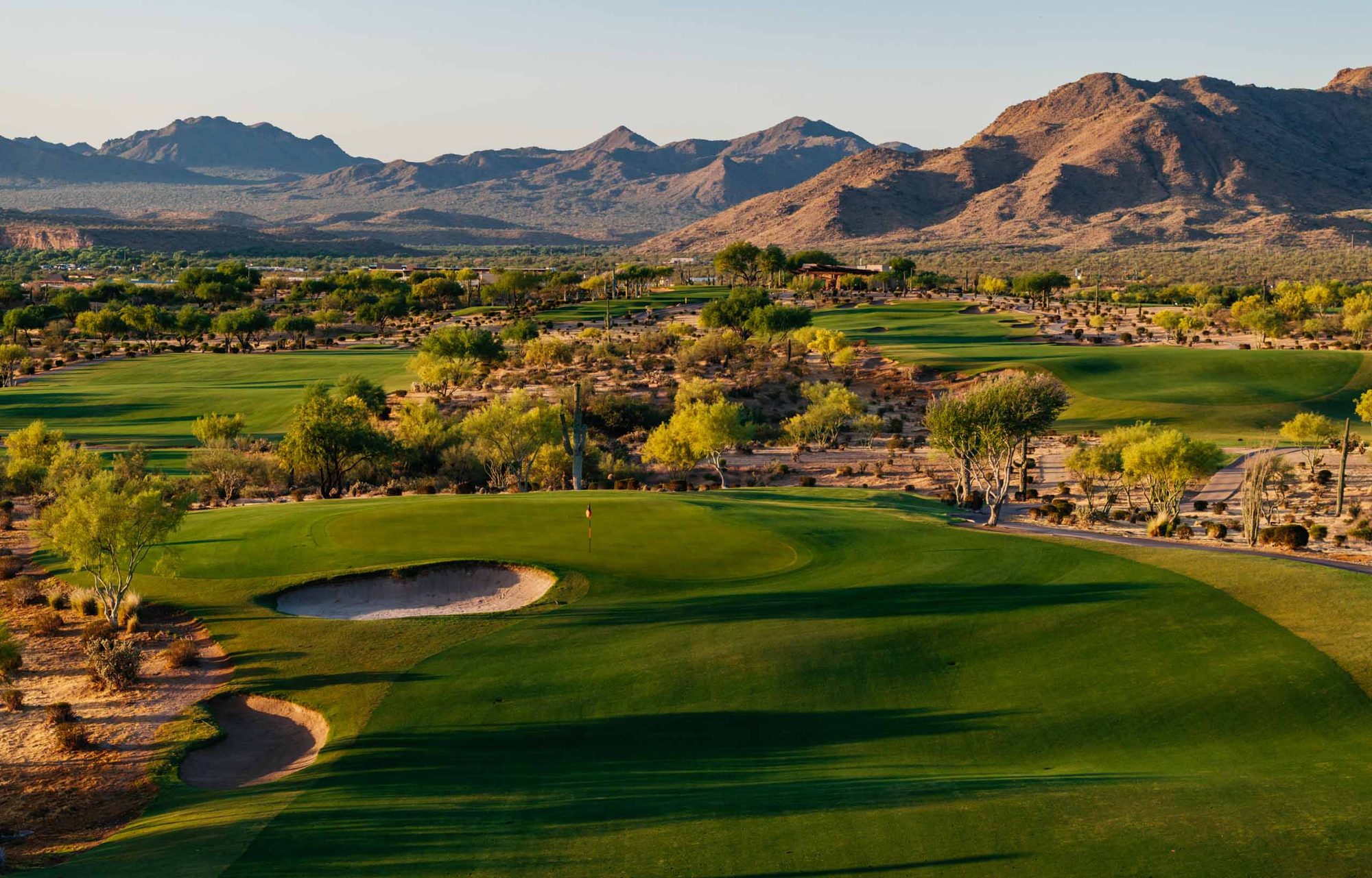 Elevated view down a We-Ko-Pa Saguaro fairway in low golden light with saguaros and bare mountains behind