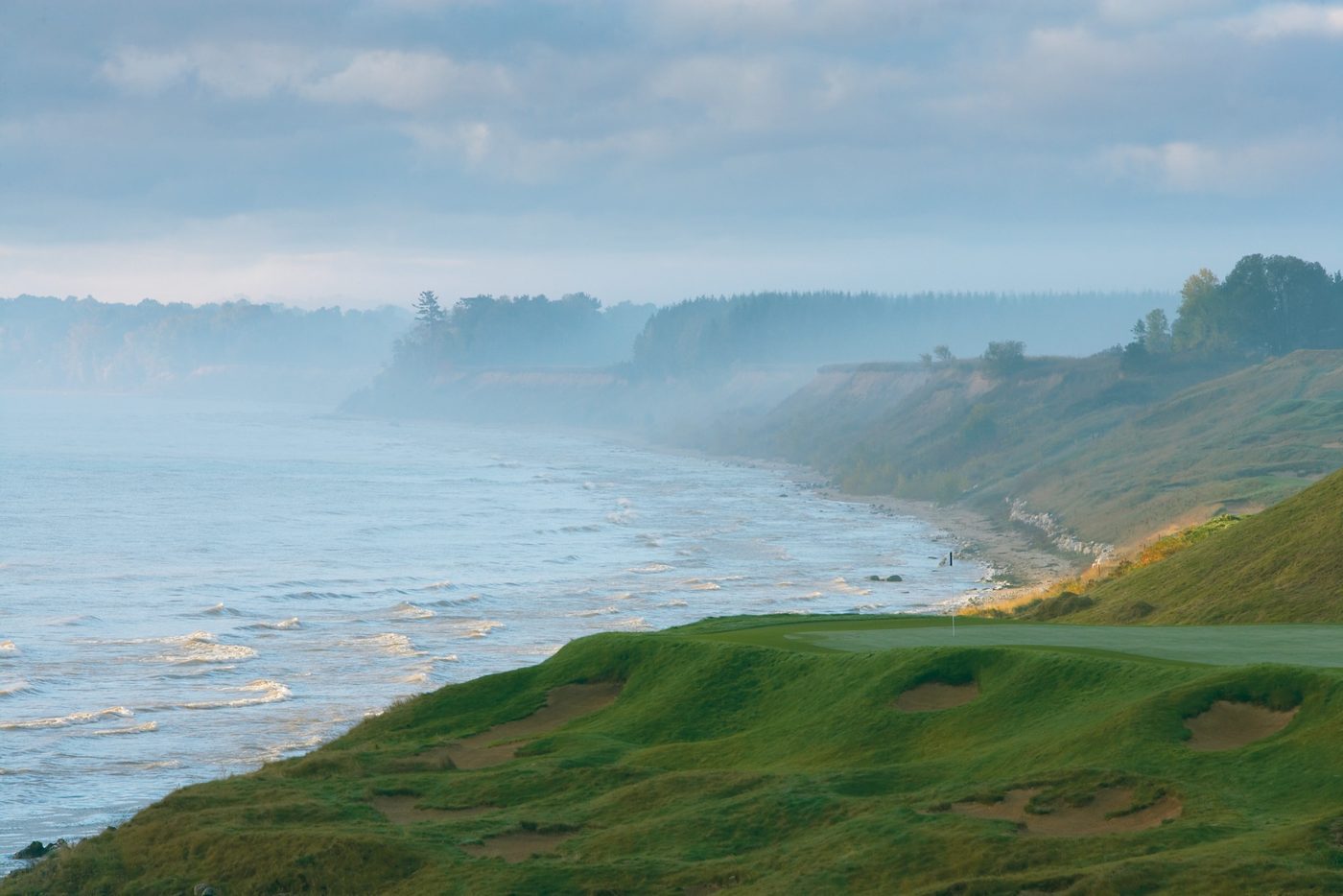 The par-3 3rd green on a bluff edge with mist over the Lake Michigan shoreline