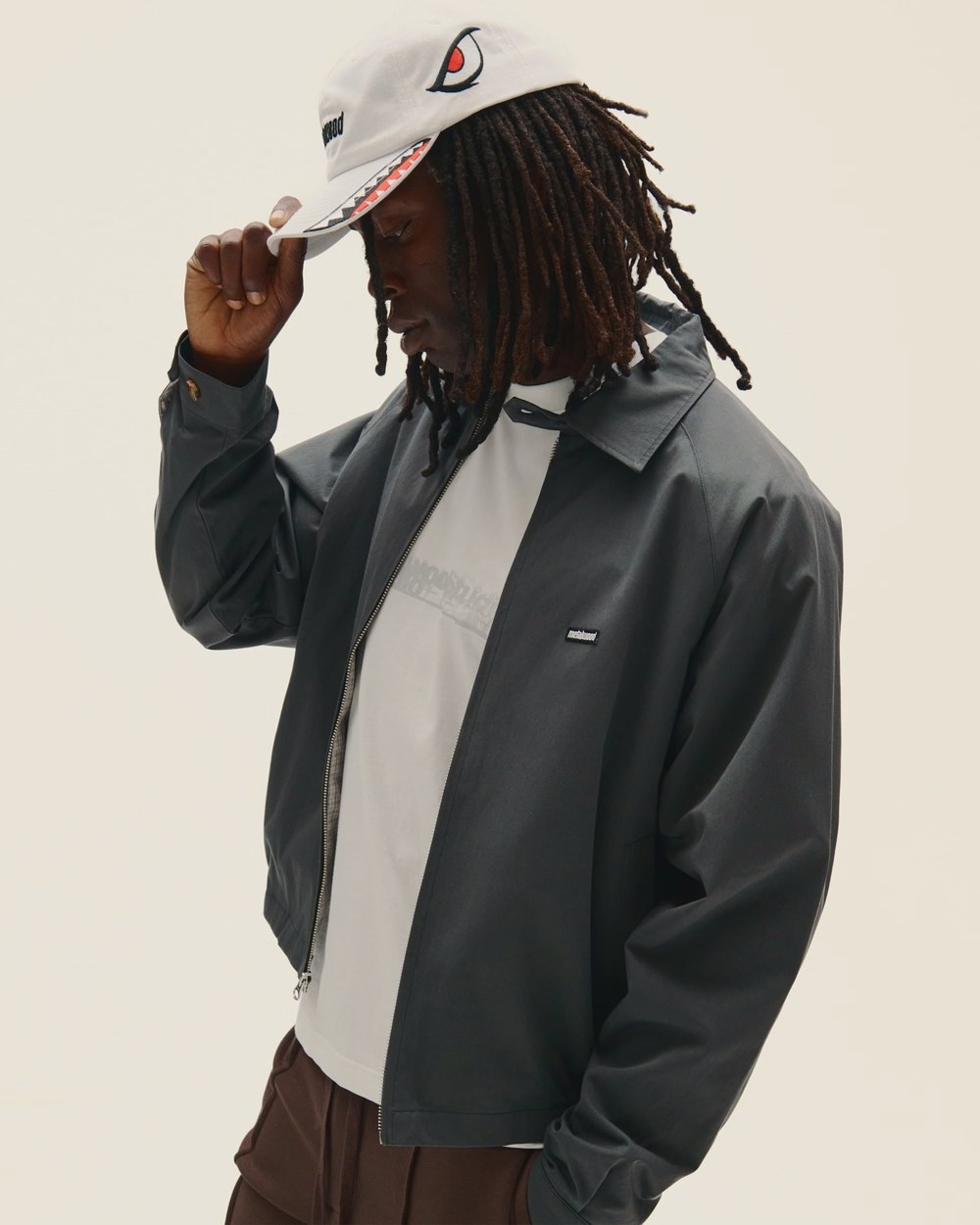 A man in the steel Raglan Sleeve Blouson tipping a white Bomber Dad Hat