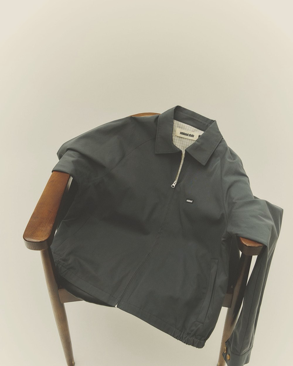 The steel Raglan Sleeve Blouson hung on a wooden chair