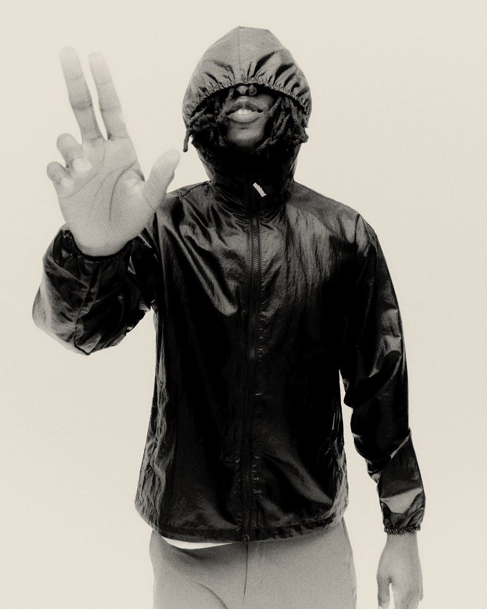 A man in the black Oasis Parka with the hood up, flashing a peace sign, in black and white