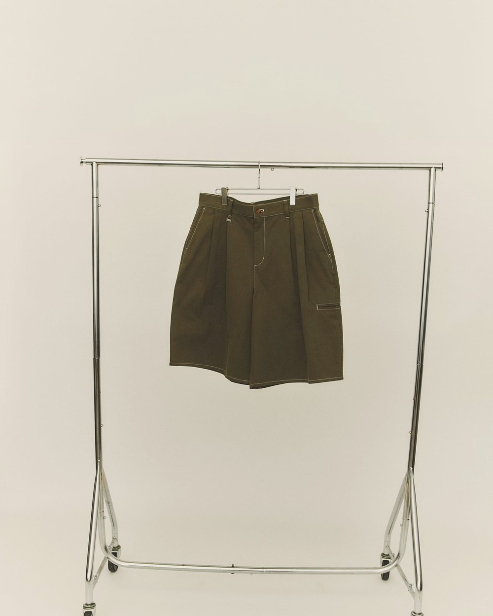 A pair of olive Buster Shorts hanging alone on a chrome clothes rail