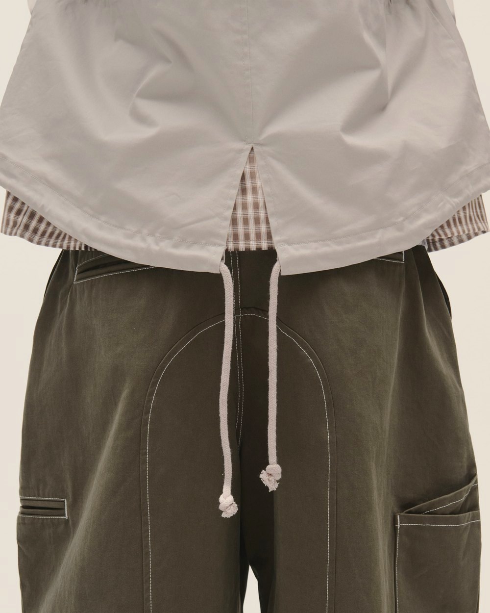Olive trousers with contrast stitching under a cream jacket with drawstring hem