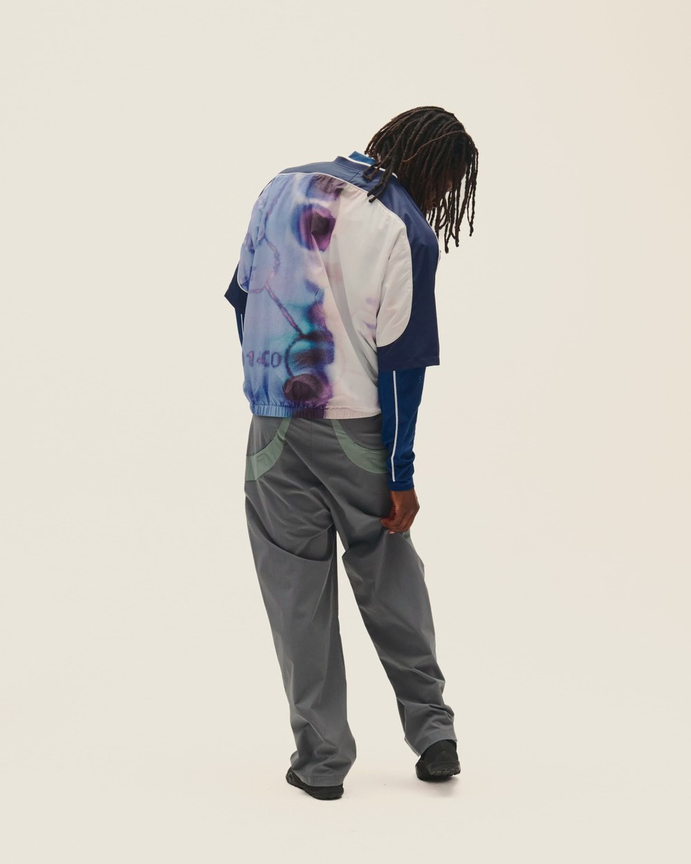 A man seen from behind in the SS V-Neck Windbreaker and gray pants