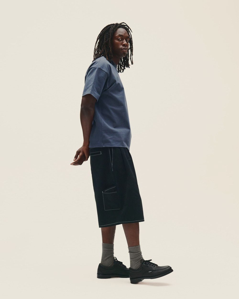 A man in a blue short-sleeve top and black shorts, side view