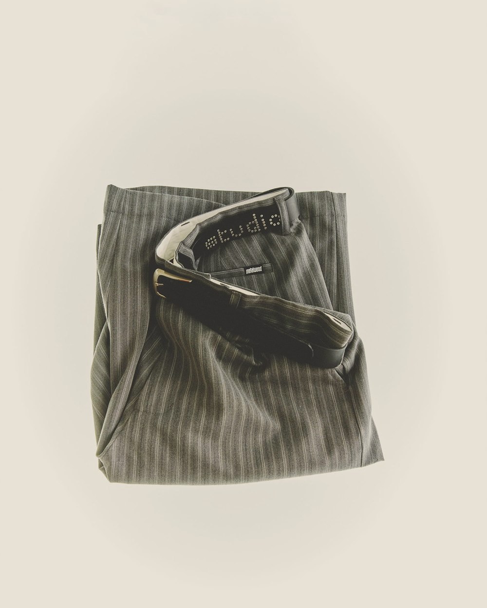 Folded pinstripe trousers with a metal belt-loop charm