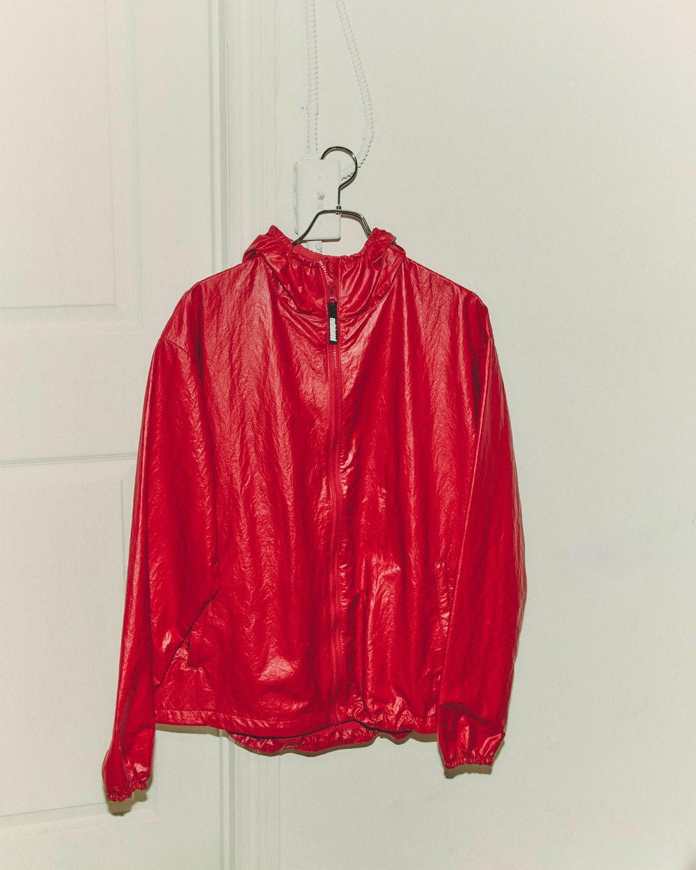 The ruby Oasis Parka hanging on a hanger against a white door