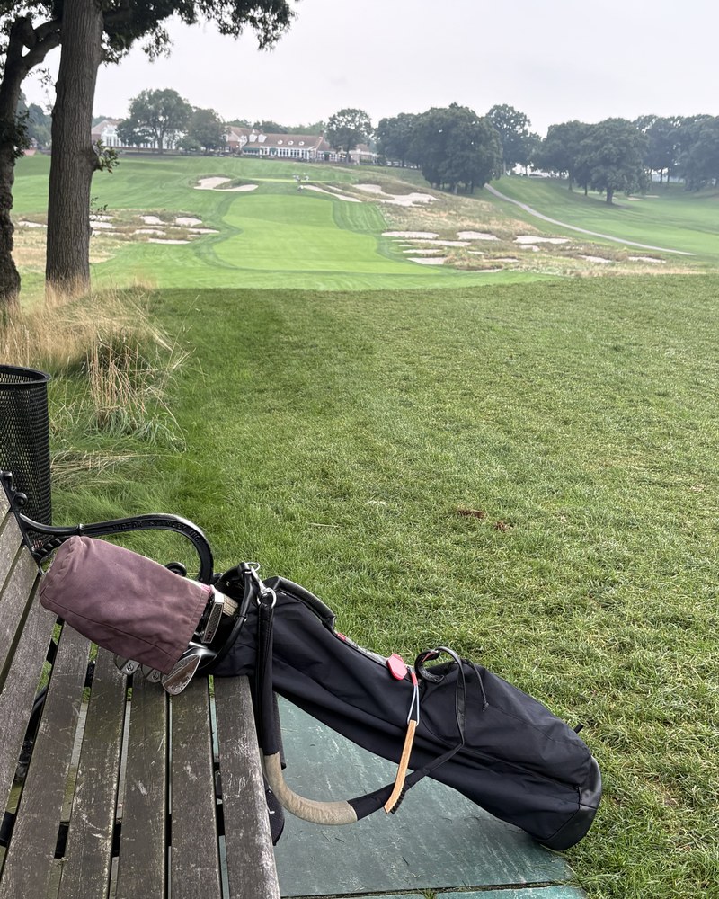 A stand bag on a bench overlooking the Bethpage clubhouse across a heavily bunkered hole