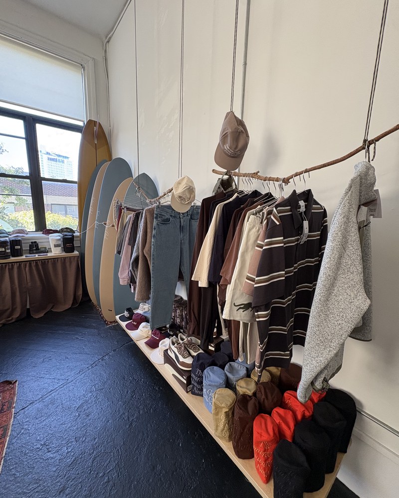 A tree branch used as a clothing rail at Gumtree, hung with striped knits and denim, caps and sneakers on the plinth below