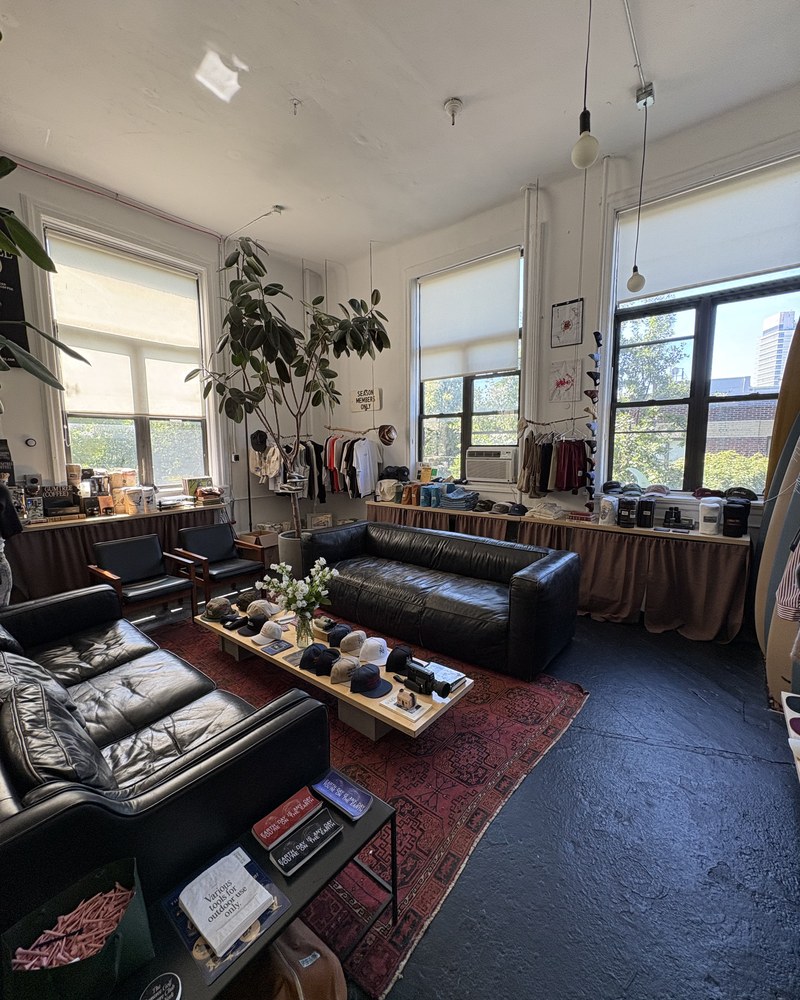 The Gumtree Golf and Nature Club studio in Greenpoint, Brooklyn — leather sofas, a rug, caps laid out on a low table and rails of clothing under tall windows