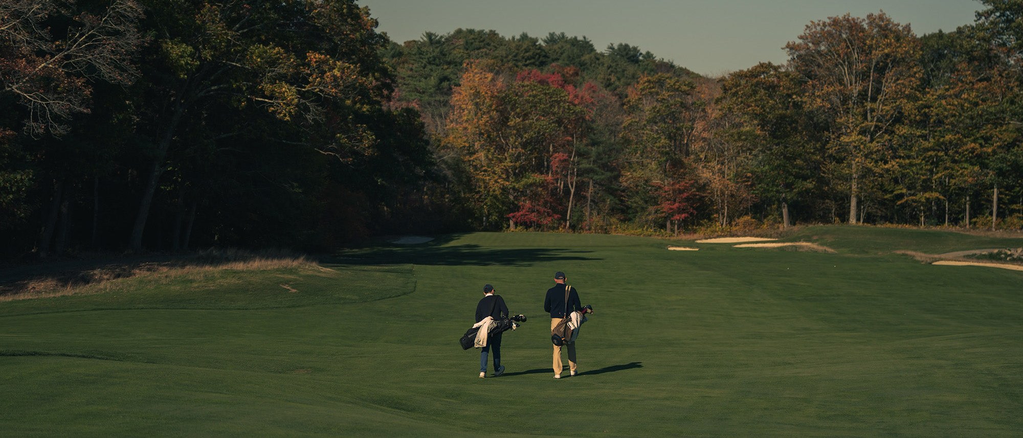 Two golfers walking a fairway with carry bags under autumn trees, from Good Walk Coffee’s own photography