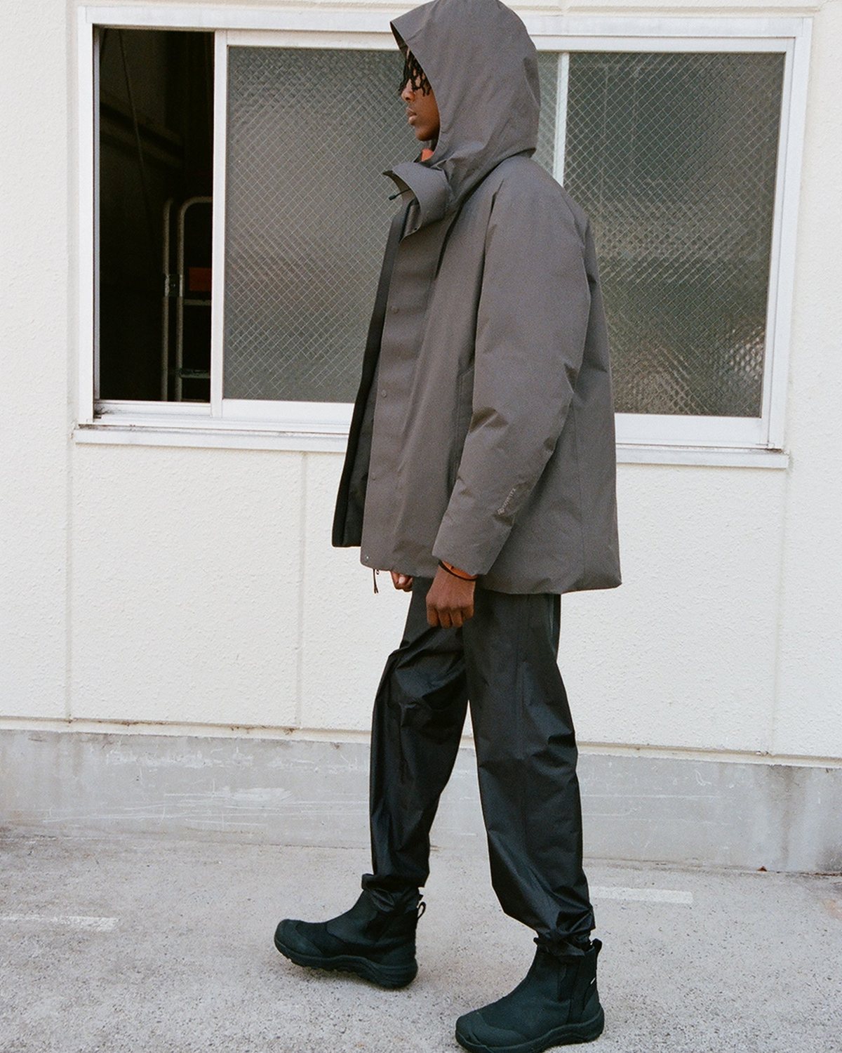 A model in a hooded shell and track pants walking past a window