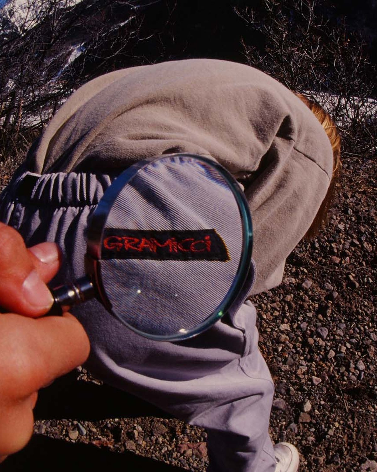 A magnifying glass held over the Gramicci label on a snowy mountain slope