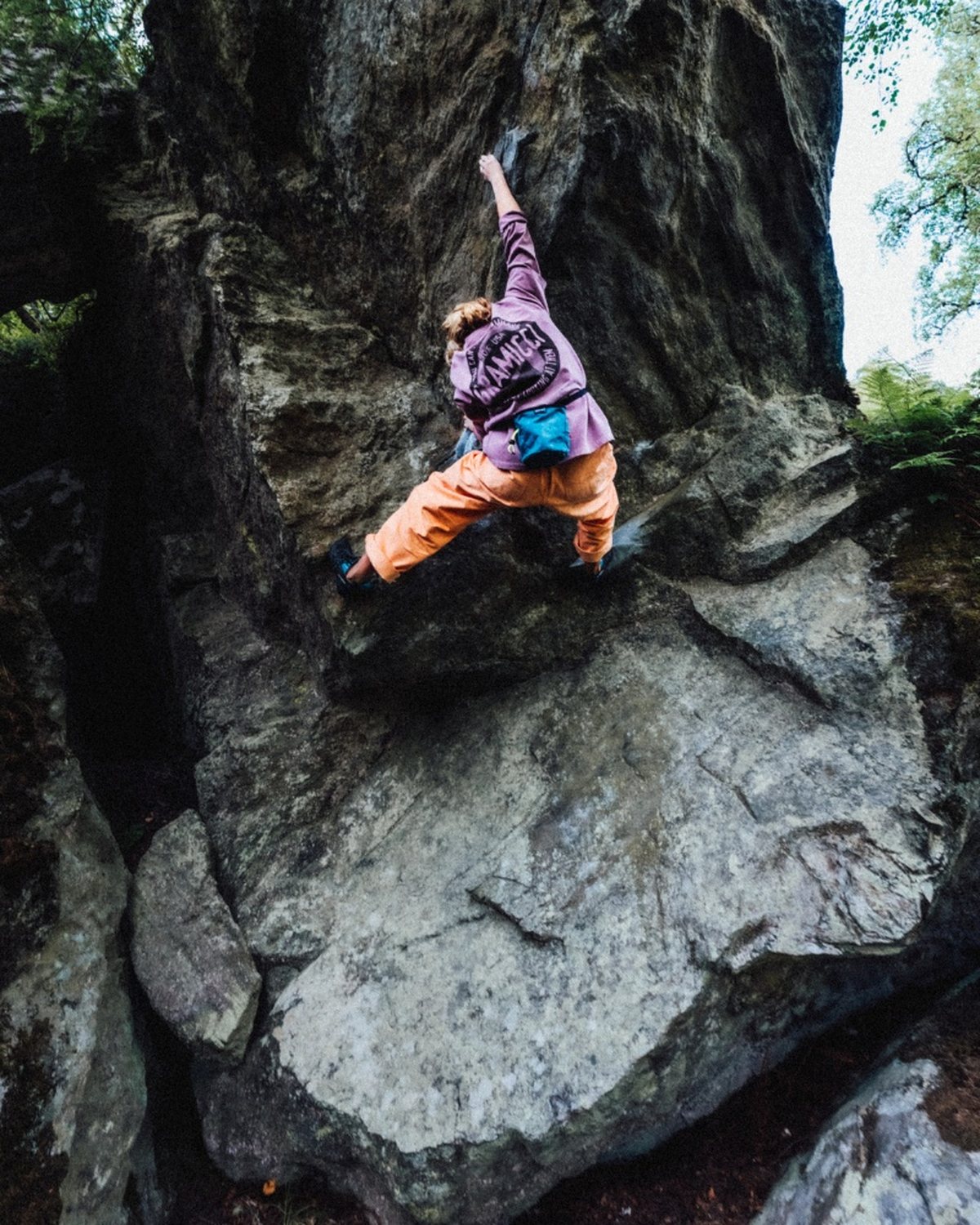 Someone bouldering an overhanging mossy rock in orange pants