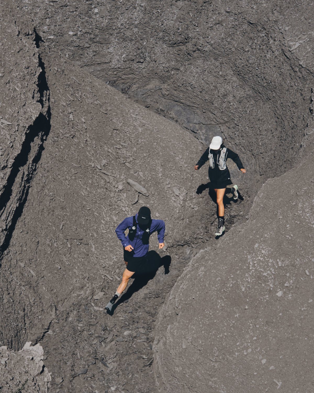 Two runners climbing a grey rock gully, shot from above