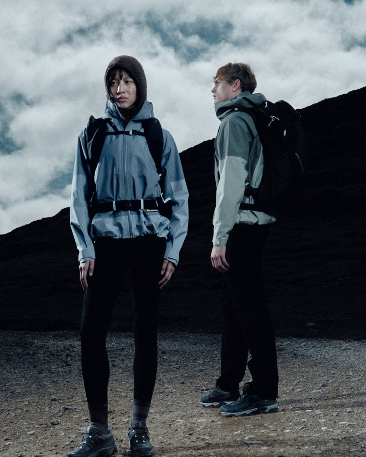 Two hikers in shells on a dark ridge under heavy cloud