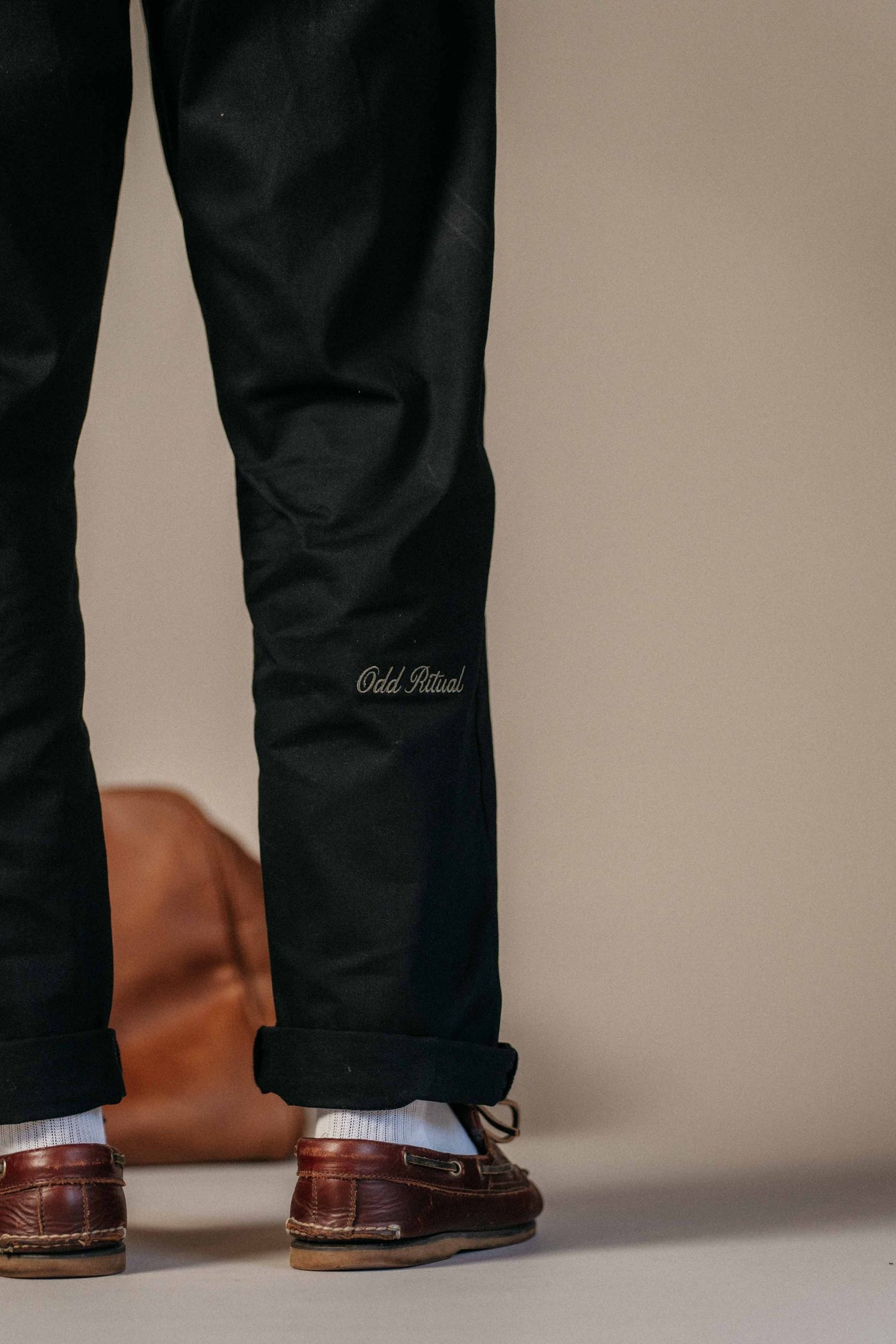 The back of the trouser leg above a rolled hem, with Odd Ritual embroidered in script