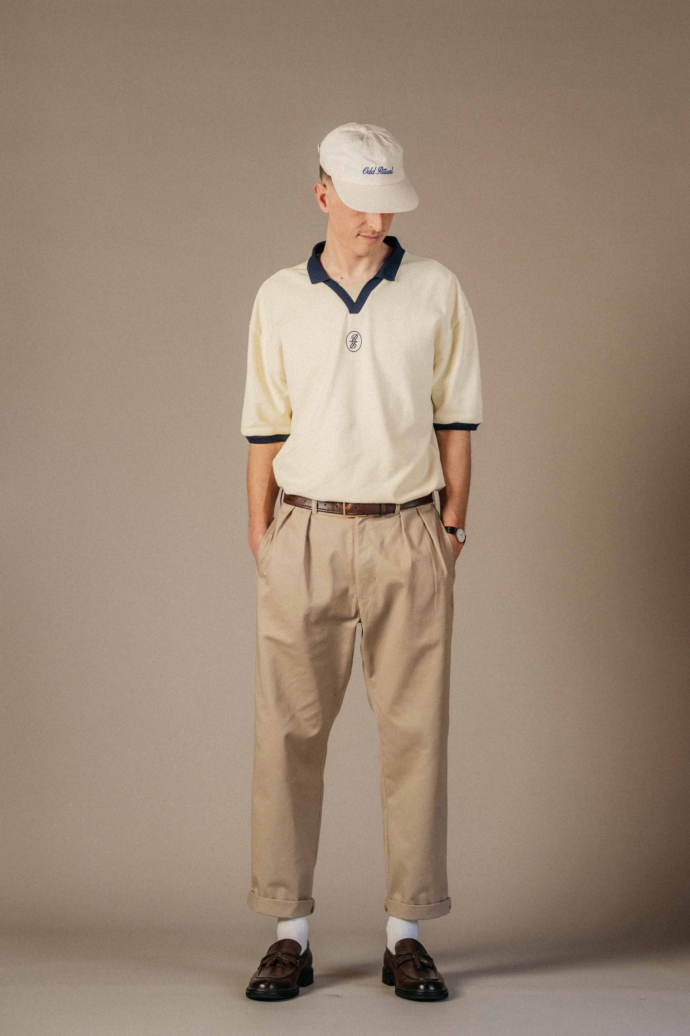 A man in a cream polo and khaki Odd Ritual Pleated Daily Trousers holding a hickory club