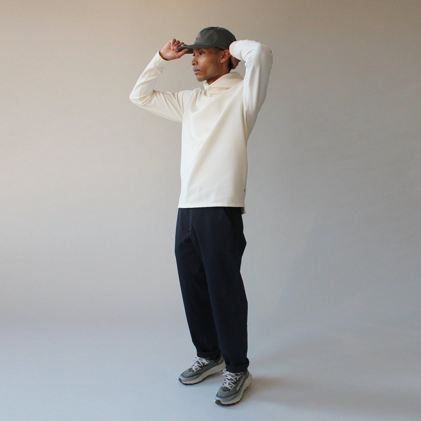 A model adjusting his cap in a cream top and dark navy Sentinel trousers