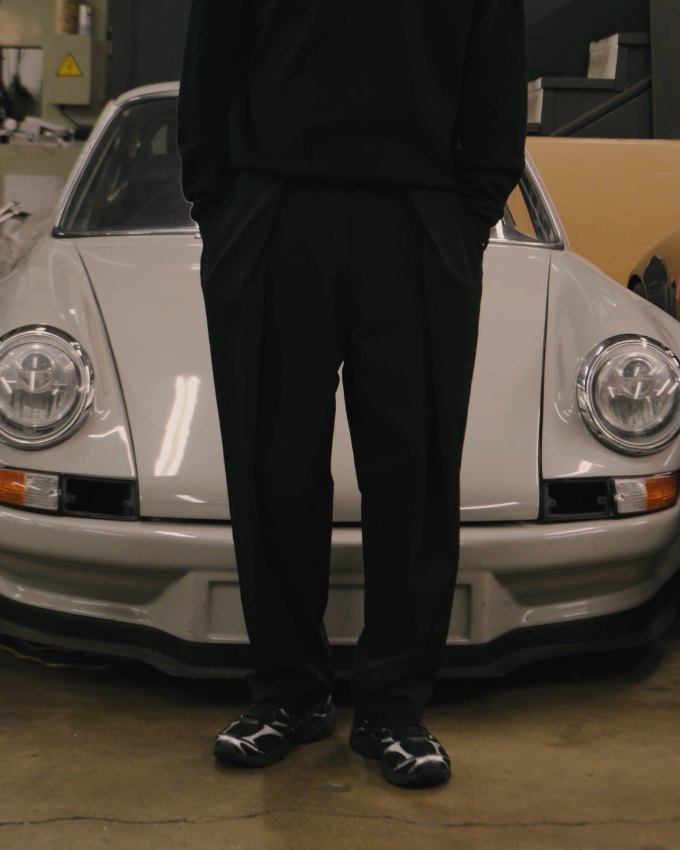 A man in black Students Science pants standing in front of a silver Porsche in a garage