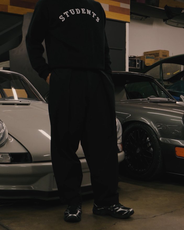A man in a Students sweatshirt and black Science pants among vintage cars
